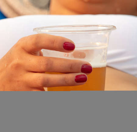 Beer in a plastic glass in the hand of a girl on the beach.の写真素材