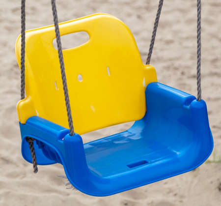 A blue and yellow seat on a children's swing. Close-up