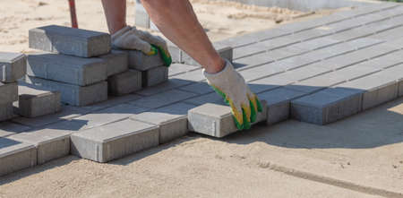 A worker lays paving slabs at a construction site.