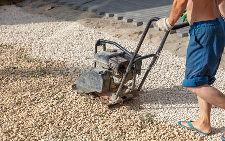 A worker lays down gravel and sand for paving slabs. Construction