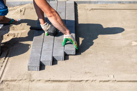 A worker lays paving slabs at a construction site.