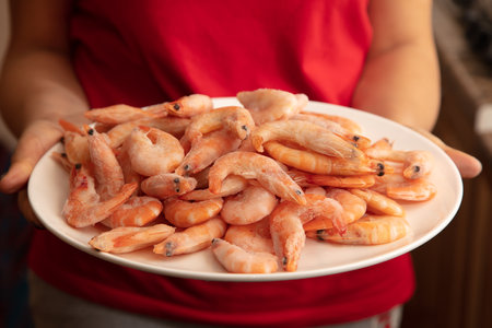 Red frozen shrimps on a white plate in the hands of a girl.の写真素材