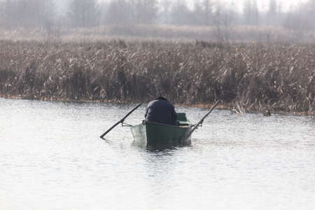 A man in a boat is fishing in a pond in the fall.の写真素材