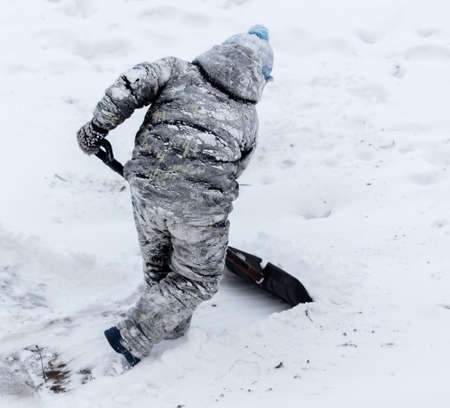A boy with a shovel cleans snow in winter.の写真素材