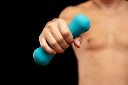 A man with a kettlebell in his hand on a black background. Sport