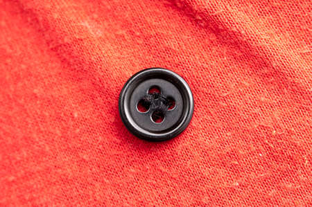 Black button on red fabric. Macroの写真素材