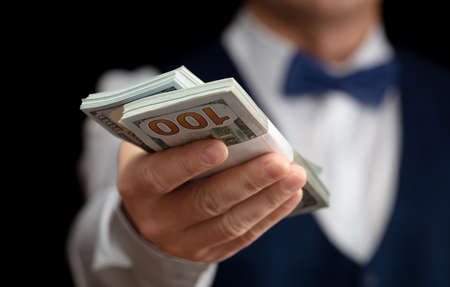 A croupier with a bundle of dollars in his hands on a black background.の写真素材