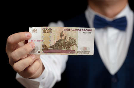 A croupier with a banknote of one hundred Russian rubles in his hands on a black background.の写真素材