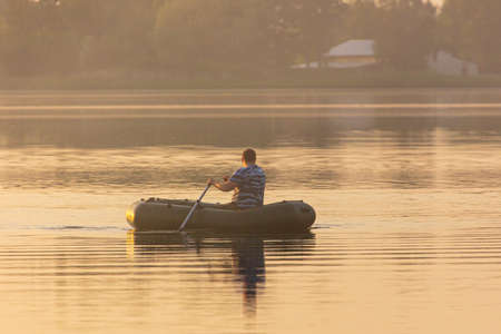 A man floats in a boat on the lake at sunset.の写真素材