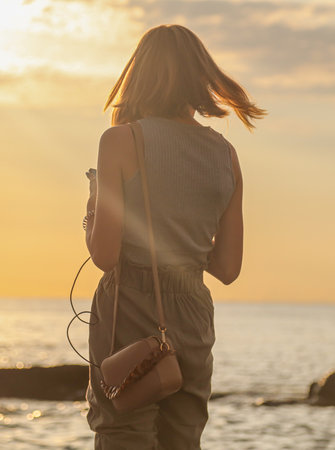 A girl from behind stands by the sea at sunset.の写真素材