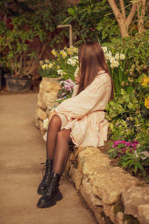 A girl in a dress sits on a stone in a spring park. Legs in black shoesの写真素材