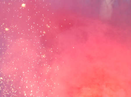 Red smoke with firework sparks in nature during the day.