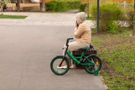 The girl is sitting on a bench with a bicycle.