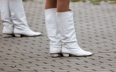 White boots on the feet of a girl standing on paving stonesの写真素材