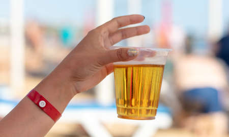 A glass of beer in the hand of a girl on the beach.の写真素材