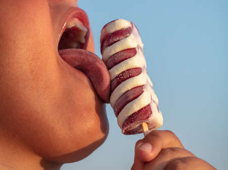 The boy licks ice cream with his tongue against the blue sky.の写真素材