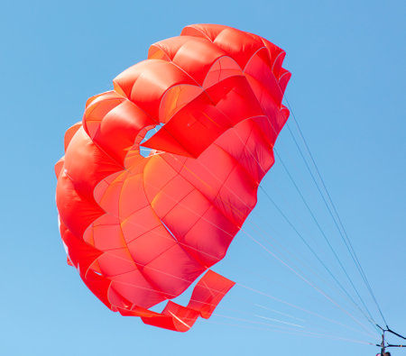 A red parachute flies in the blue sky.