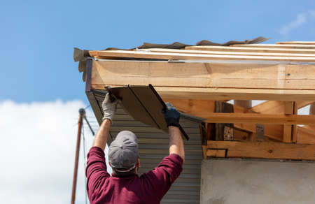Workers install metal roofing on the wooden roof of a house. Technology