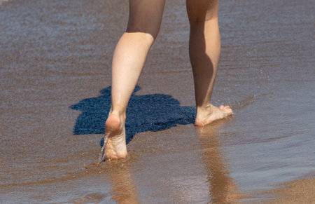 Legs of a woman walking along the shore by the sea.