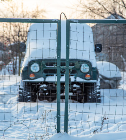 Car covered with snow in winter behind a fenceの写真素材