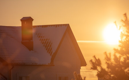House with snow on the roof at sunset. Winter