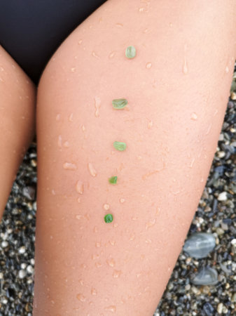 Green sea pebbles on the skin of the girl's leg. close-upの写真素材