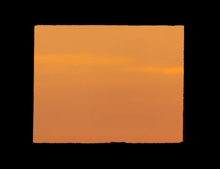 Black silhouette of a window in the wall of the house on the background of the sunset.