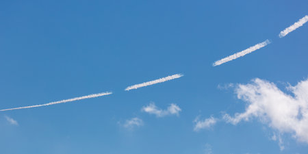 White lines from an airplane against a blue sky.の写真素材