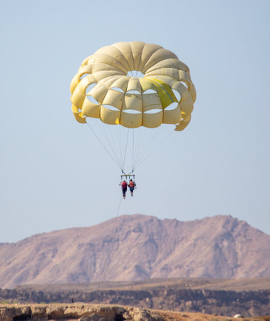 A yellow parachute flies in the sky over the mountains.