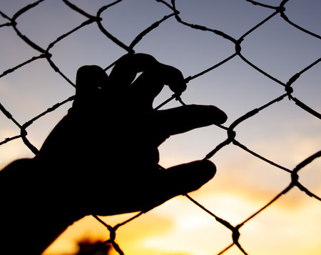 Man's hand on the fence grid at sunset. backgroundの写真素材