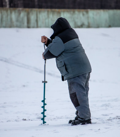 A fisherman drills a hole in the ice in winter.の写真素材