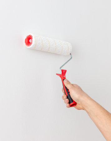 A worker paints the walls in a room with white paint with a roller. Repair in the house.の写真素材