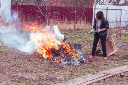 A young woman in a black jacket burns dry grass in the yard.の写真素材