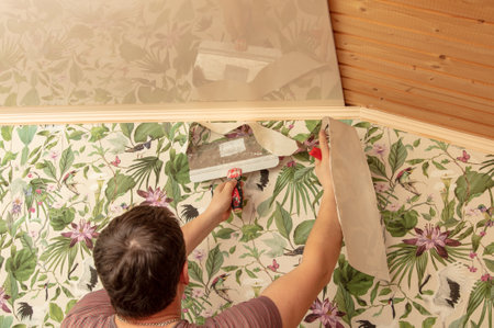 A worker pastes wallpaper on the walls in a room.