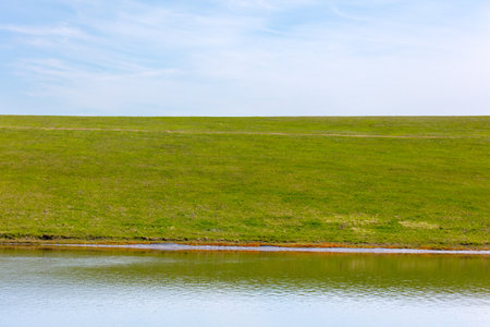 Spring landscape with a pond in the middle of green grass and blue sky.の写真素材