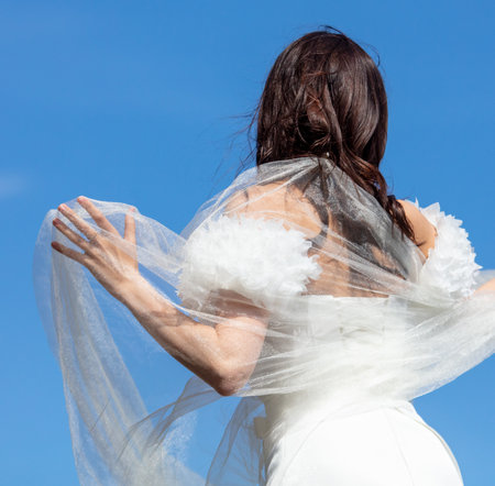 A girl in a wedding dress against a blue sky. back viewの写真素材