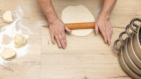 Close-up of an elderly woman rolling dough with a rolling pin.