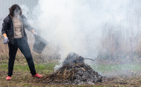 A young woman in a black jacket burns dry grass in the yard.の写真素材