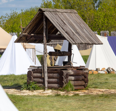 Wooden well on the background of a white tent in the field.の写真素材