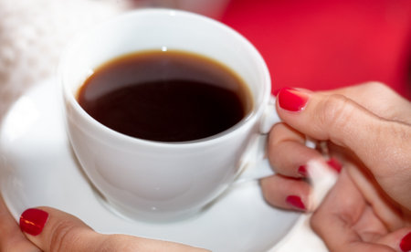 Female hands with red manicure holding a cup of hot coffee.の写真素材