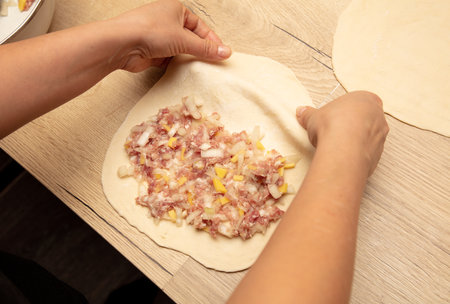 Preparing pizza dough with meat, onions and spices on wooden table.の写真素材