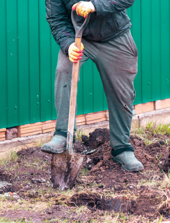 A worker digs the ground with a shovel to install a fence.の写真素材