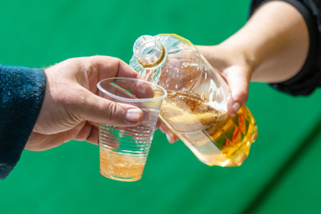Man and woman hands holding plastic bottle with yellow liquid on green background.の写真素材