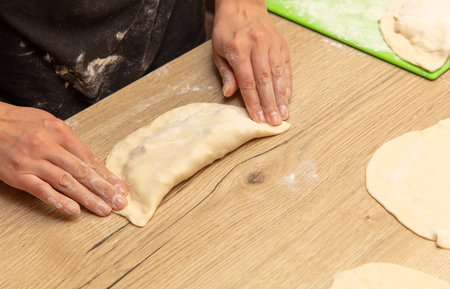A woman prepares pies from dough and minced meat on the table.の写真素材