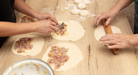 Women prepare pies from dough and minced meat on the table.