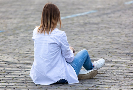 The girl is sitting on the paving stones.