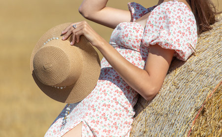 A girl in a dress with a hat near a haystack.の写真素材