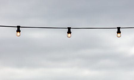 Festive light bulbs shine against the background of the sky with clouds.