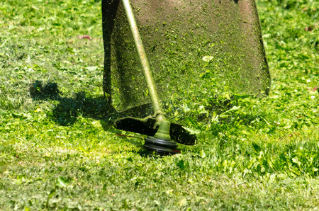 A man mows green grass with a petrol trimmer.