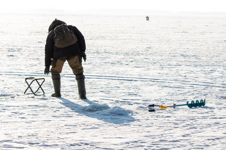 A man with a drill on the ice while fishing.の写真素材
